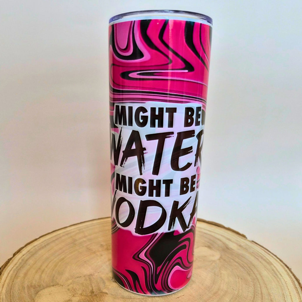 A tall, slim tumbler with a pink, black, and white marbled pattern and the text 'MIGHT BE WATER MIGHT BE VODKA' in bold black letters, displayed on a round wooden slice against a plain light background.