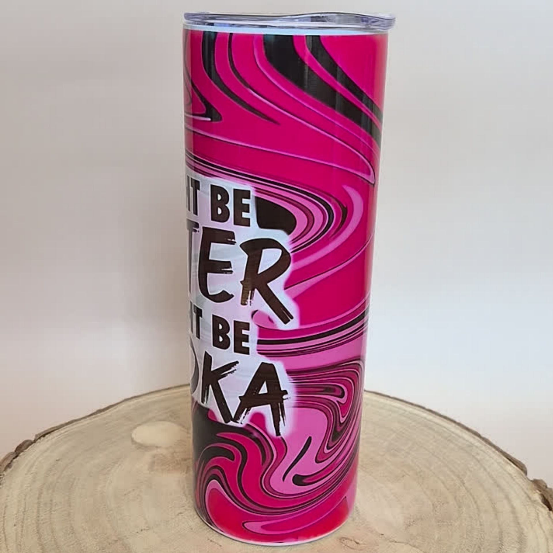 A tall insulated tumbler with a pink, black, and white marbled swirl pattern and the text 'IT BE TIER NOT BE VOKA' in black and white lettering. The tumbler is shown standing on a rustic wood slice against a plain light background.