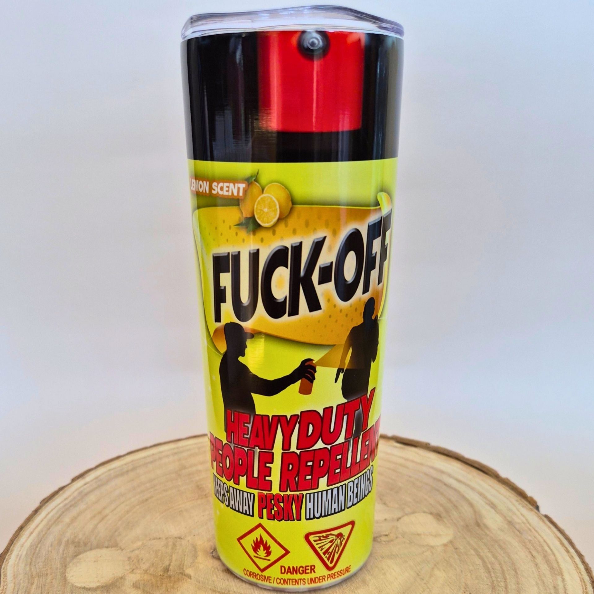 A can of 'FUCK-OFF' heavy duty people repeller spray, featuring a bright yellow label with black and red text, set on a wooden slice against a white background