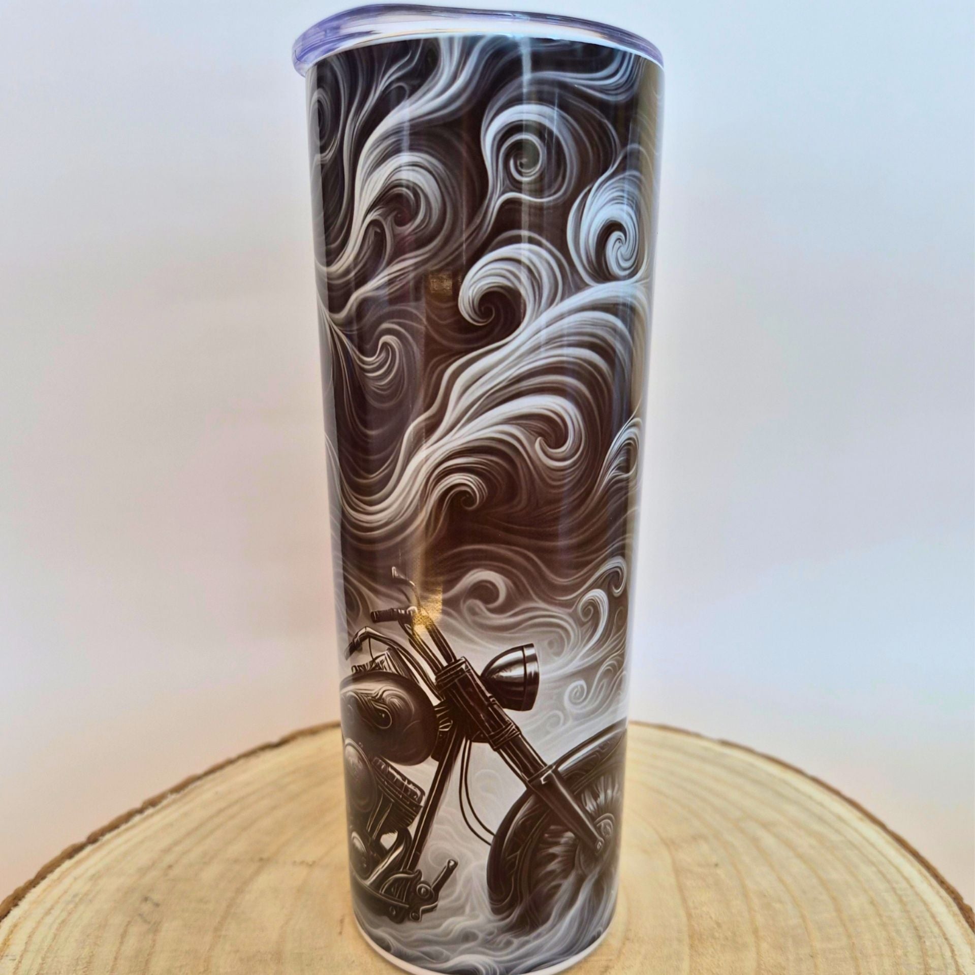 A tall insulated tumbler with a clear lid, featuring a black and white swirling wave design with a motorcycle graphic near the bottom, displayed on a wooden slice against a light background with 'Memory Metal' watermarks.