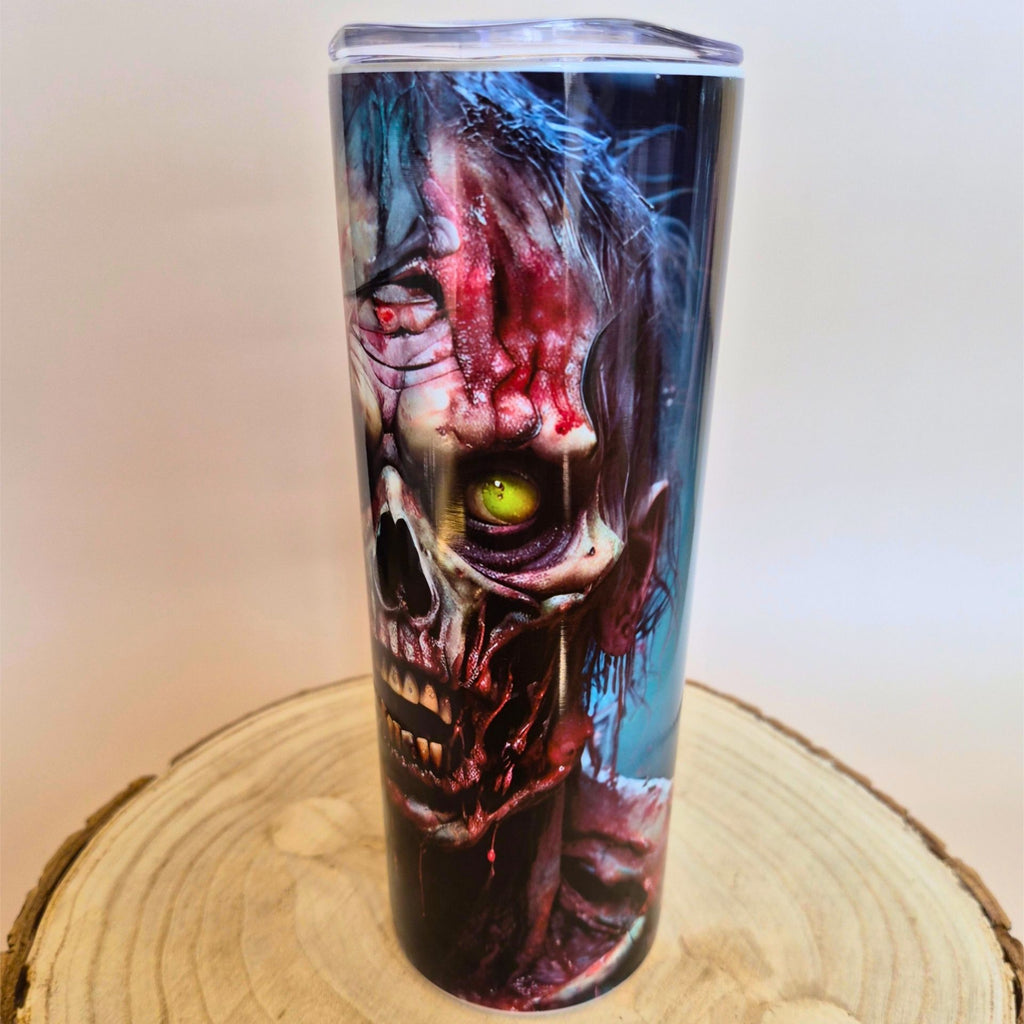 A tall insulated tumbler with a clear lid, featuring a detailed zombie skull graphic with a glowing green eye. The tumbler is displayed on a wooden slice coaster against a light beige background with 'Memory Metal' watermarks.