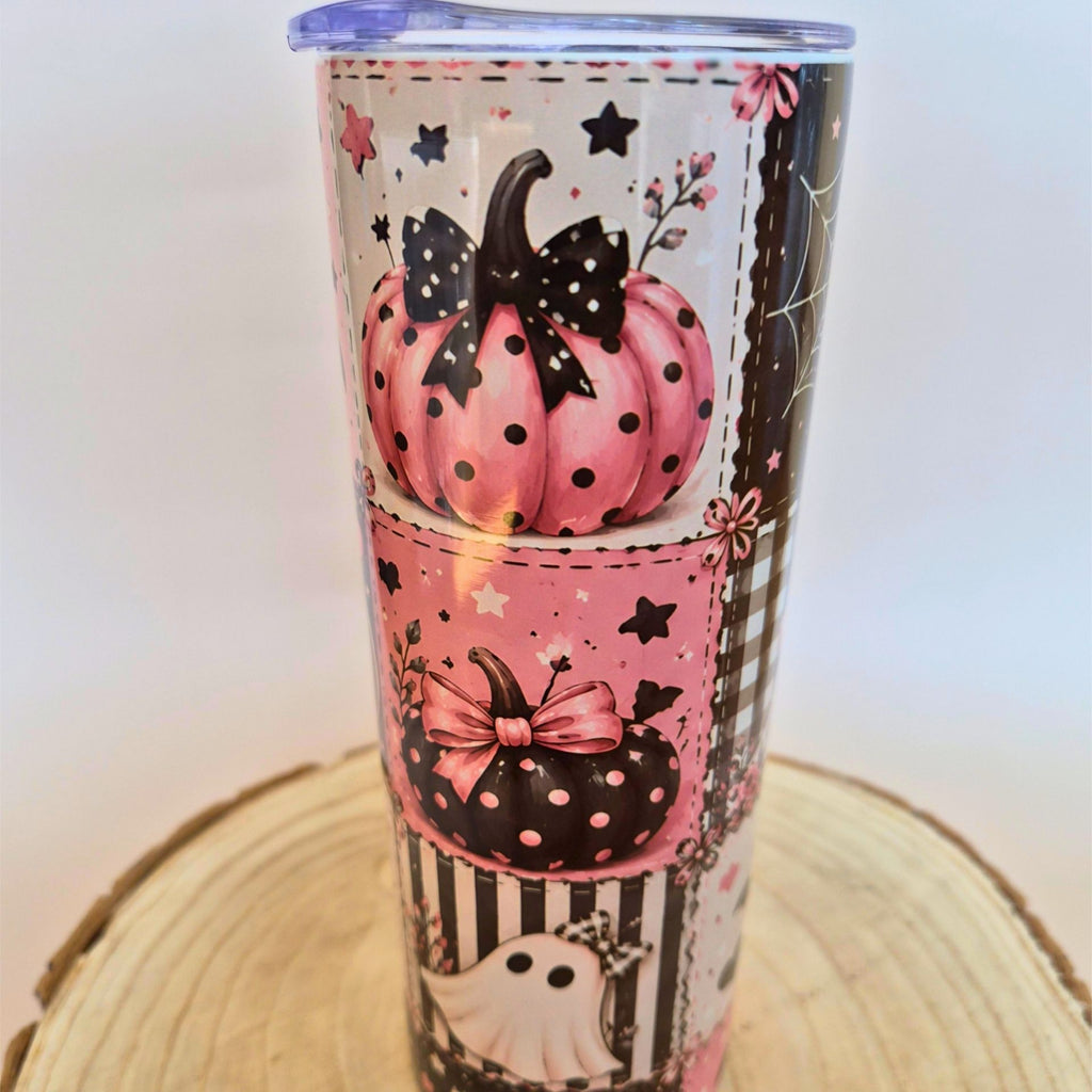 A tall insulated tumbler with a Halloween-themed print featuring pink and black polka-dot pumpkins, black bows, stars, stripes, and a ghost, shown on a wooden slice coaster against a plain light background.